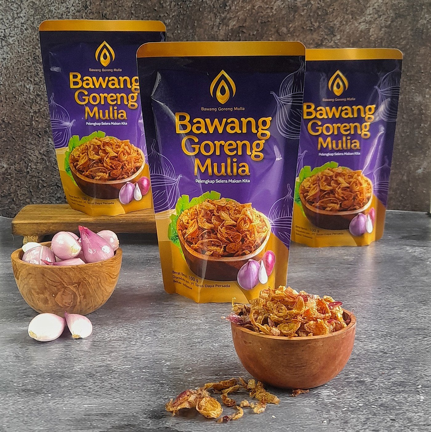 Tiga kemasan pouch Bawang Goreng Mulia bersama bawang merah dan semangkuk bawang goreng